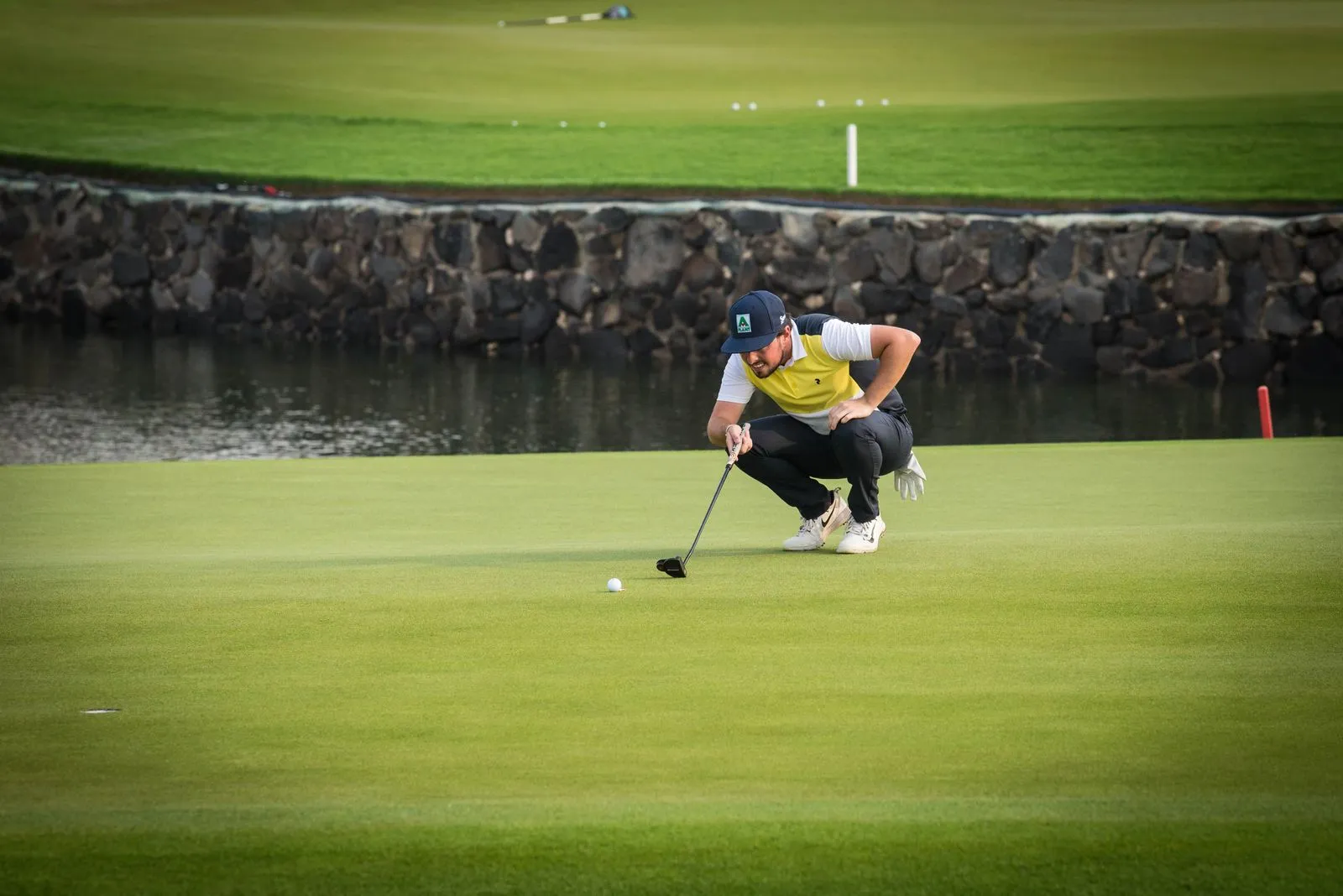 Golfer crouches to line up a putt on a sunny golf course morning.